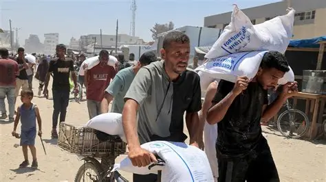 Gaza Conflict Humanitarian Crisis — civilians carrying WFP aid sacks during food distribution