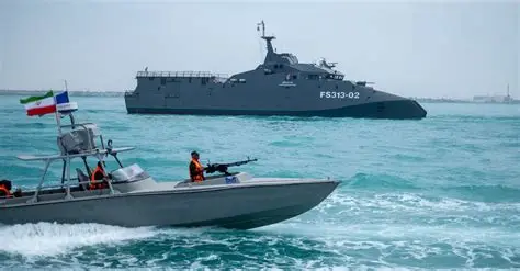 Iranian patrol boat with armed personnel sailing near a larger military vessel during naval operations in regional waters