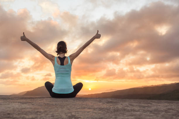 Person sitting cross‑legged at sunrise with arms raised, expressing calm, freedom and emotional balance against a scenic horizon