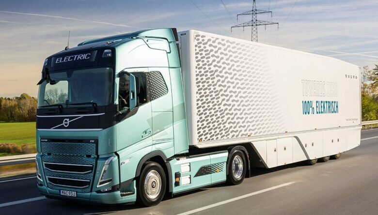 Volvo FH Electric truck driving on a highway, featuring blue cab and ‘Towards Zero 100% Electric’ trailer design