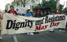 May Day protesters march through a city street holding a large “Dignity and Resistance” banner during nationwide demonstrations.