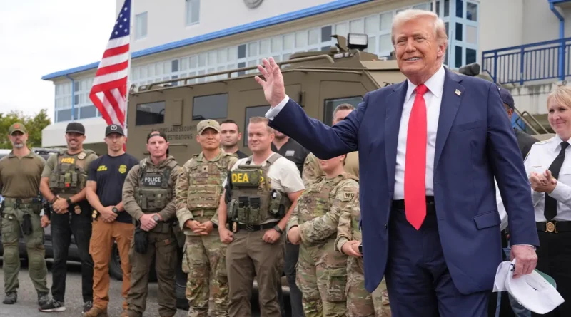 U.S. President Donald Trump waves while standing with Homeland Security officers in front of an armored vehicle during a security visit.