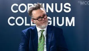 Speaker in a blue suit with a green striped tie during an event at Corvinus Collegium.