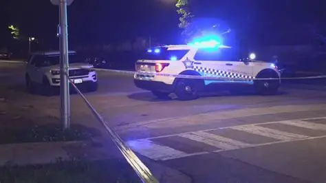 A nighttime police scene in Chicago with flashing emergency lights, a cordoned‑off street, and officers securing the area after a shooting incident.