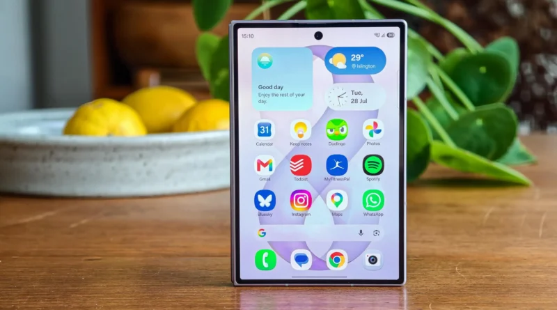 Samsung Galaxy Z Fold 8 home screen displayed on a wooden surface with apps and widgets visible.